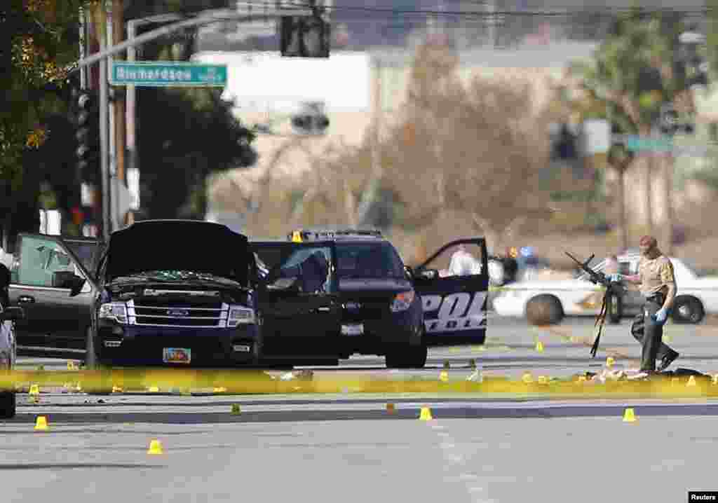 A police officer picks up a weapon from the scene of the investigation around the area of the SUV vehicle where two suspects were shot by police following a mass shooting in San Bernardino, California. Authorities were working to determine why Syed Rizwan Farook 28, and Tashfeen Malik, 27, opened fire at a holiday party of his co-workers in Southern California, killing 14 people and wounding 17 in an attack that appeared to have been planned.