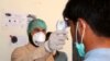 FILE - A health worker takes the temperature of a man who returned from Iran and is under medical observation, at the border post in Taftan, Pakistan, Feb. 25, 2020.