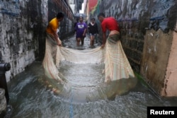 FILE - Men use a mosquito net to catch fish in a flooded alley in a residential district in Bacoor, near Manila, Phillippines, Aug. 20, 2013.