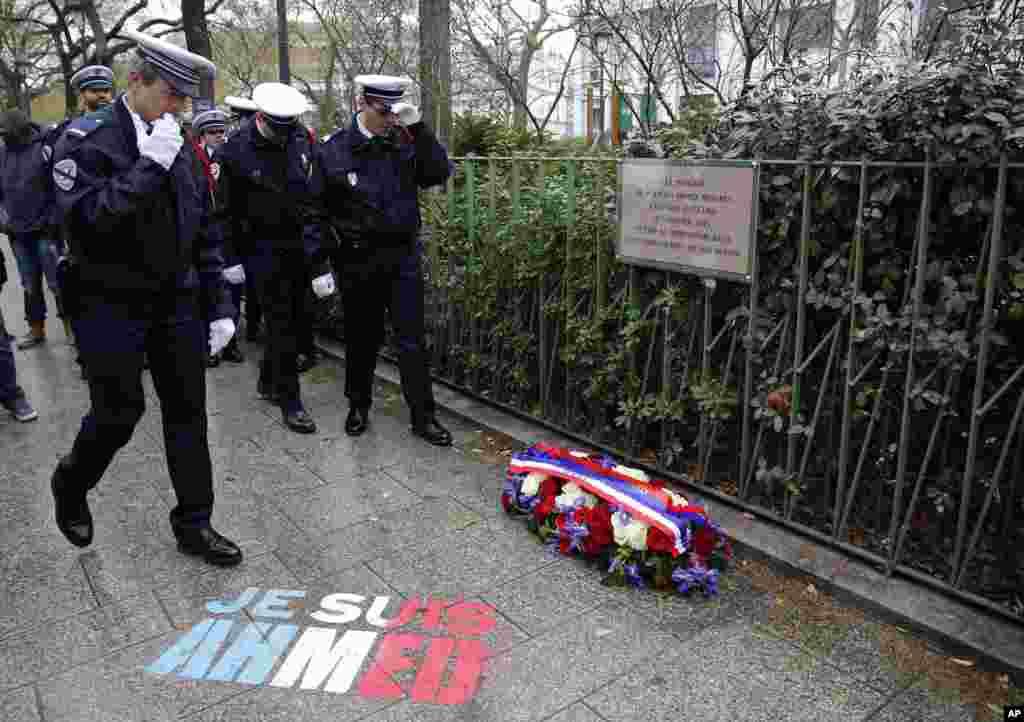 Policemen walk past &ldquo;Je suis Ahmed,&quot; or &quot;I am Ahmed,&rdquo; spray painted on the sidewalk, in the red, white and blue colors of the French flag near a plaque commemorating late police officer Ahmed Merabet in Paris, France. President Francois Hollande honored 17 victims killed in Islamic extremist attacks on the satirical newspaper Charlie Hebdo, a kosher market and police a year ago this week.
