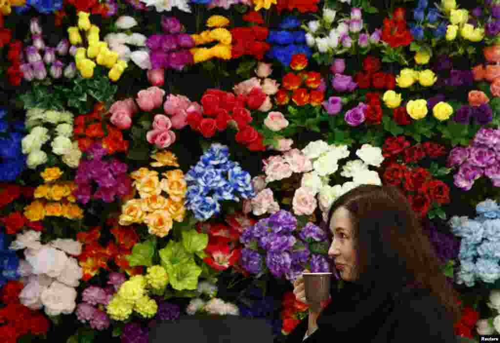 A woman drinks coffee at a stand with artificial flowers during the "Memorial and Stone Working-2015" exhibition in Minsk, Belarus.