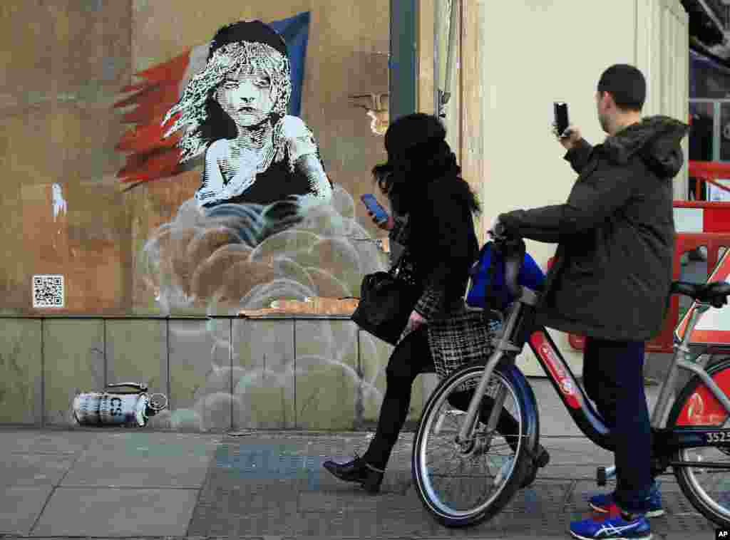 Commuters take photos on their phones of an artwork by British artist Banksy opposite the French Embassy in London.