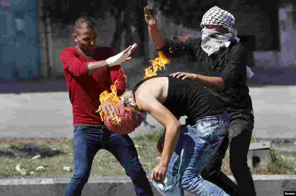 Palestinian protesters put out a fire on a compatriot caused by a molotov cocktail he was trying to hurl at Israeli troops during clashes in the West Bank city of Hebron. Seven Israelis and 27 Palestinians, including nine alleged attackers and eight children, have died in almost two weeks of street attacks and security crackdowns.