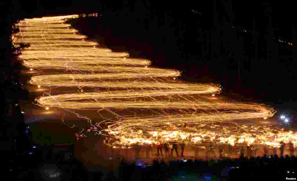 Spectators (bottom) watch hundreds of skiers descend from a slope while holding torches in the town of Zheleznogorsk, northeast of Krasnoyarsk, Siberia, Russia, Feb. 27, 2016.