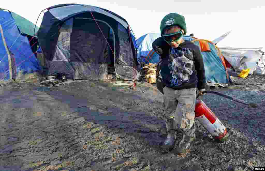 A young migrant pulls a fire extinguisher in a muddy field at a camp of makeshift shelters for migrants and asylum-seekers from Iraq, Kurdistan, Iran and Syria, called the Grande Synthe jungle, near Dunkirk, France.