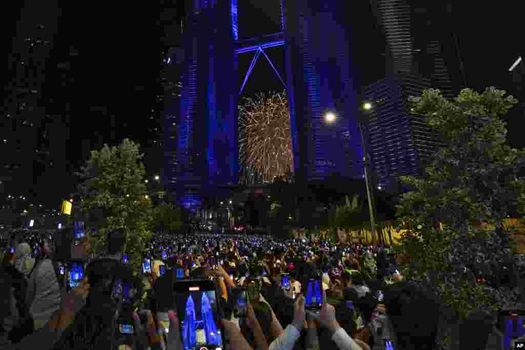 Orang-orang mengambil foto kembang api yang meledak di dekat Menara Kembar Petronas dengan ponsel pintar, selama perayaan Tahun Baru di Kuala Lumpur, Malaysia, 1 Januari 2025.
