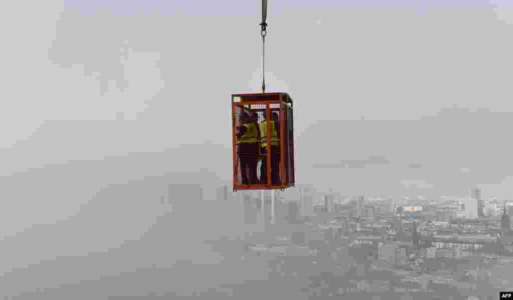 Journalists hang in a cage over fog-covered Frankfurt am Main in central Germany to watch the construction site of the Henninger tower.