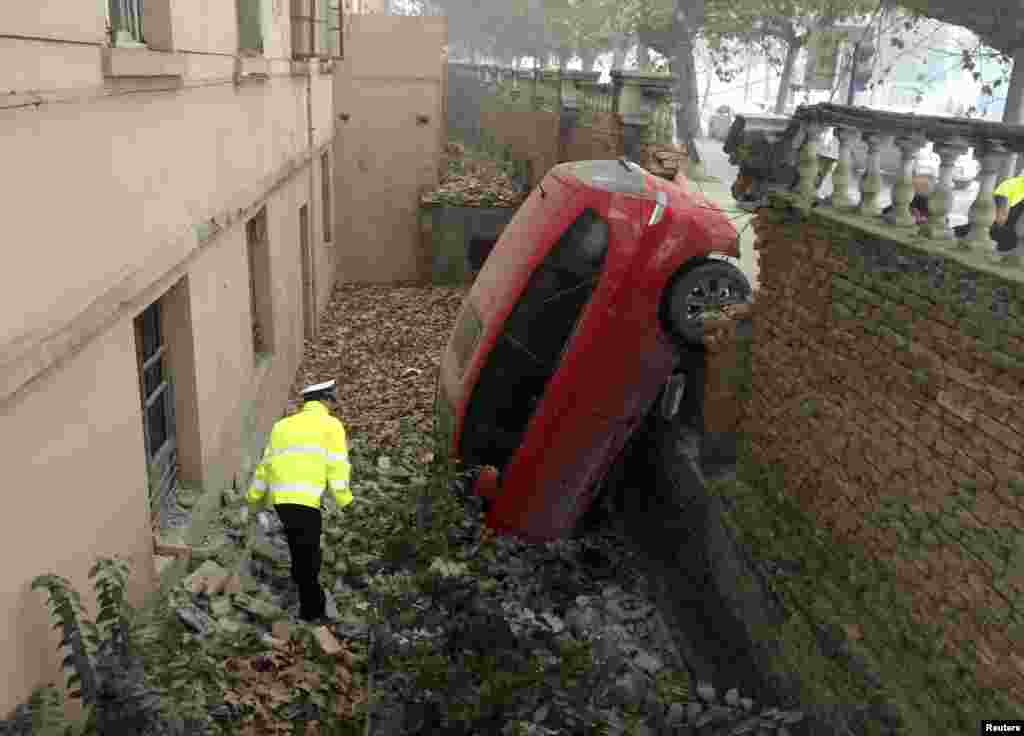 A policeman looks at a car which fell into a pit after crashing through a brick wall, on a hazy day in Xianyang, Shaanxi province, China, Nov. 30, 2015.
