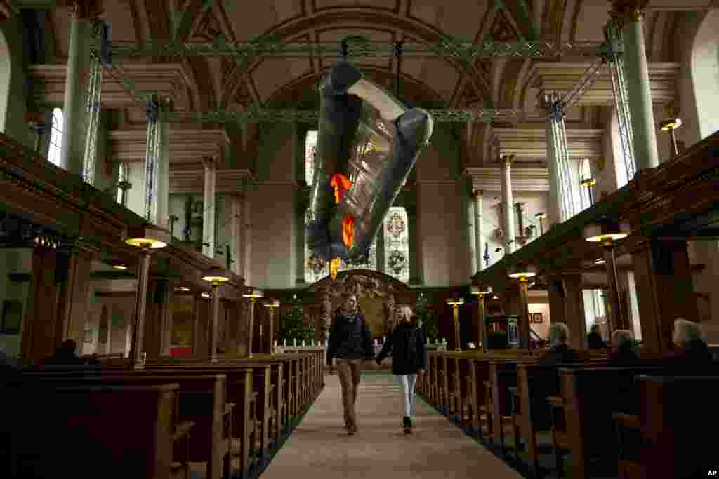 Tourists walk holding hands together beneath a salvaged dinghy with three life jackets - an installation entitled 'Flight' by artist Arabella Dorman - hanging in the nave of St. James’s Church, Piccadilly, in London.