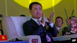 FILE - Wanda Chairman Wang Jianlin applauds in front of the logo for Dalian Wanda Group during an event at a hotel in Beijing, China, June 19, 2013.
