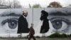 FILE - An Afghan man wearing a protective face mask walks past a wall painted with images of Zalmay Khalilzad, U.S. envoy in Afghanistan, and Mullah Abdul Ghani Baradar, the leader of the Taliban delegation, in Kabul, Afghanistan, April 13, 2020.