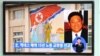 Passersby watch a local television broadcast in Seoul on May 2, 2013 showing a report and picture of Kenneth Bae (R), a Korean-American tour operator detained in North Korea, against the background of a North Korean flag painted on the wall of a building 