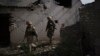 FILE - Ukrainian government soldiers walk past a destroyed home near the line separating Ukrainian forces from Russia-backed separatist rebels, near Donetsk, Ukraine, May 4, 2021.
