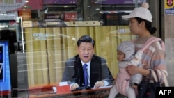 资料照片：在台湾新北市，一位母亲带着孩子经过一台电视，上面显示中国领导人习近平就台湾问题发表讲话。（2019年1月2日）