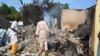 Residents watch as two men walk amidst rubble after Boko Haram militants raided the town of Benisheik, west of Borno State capital Maiduguri September 19, 2013.