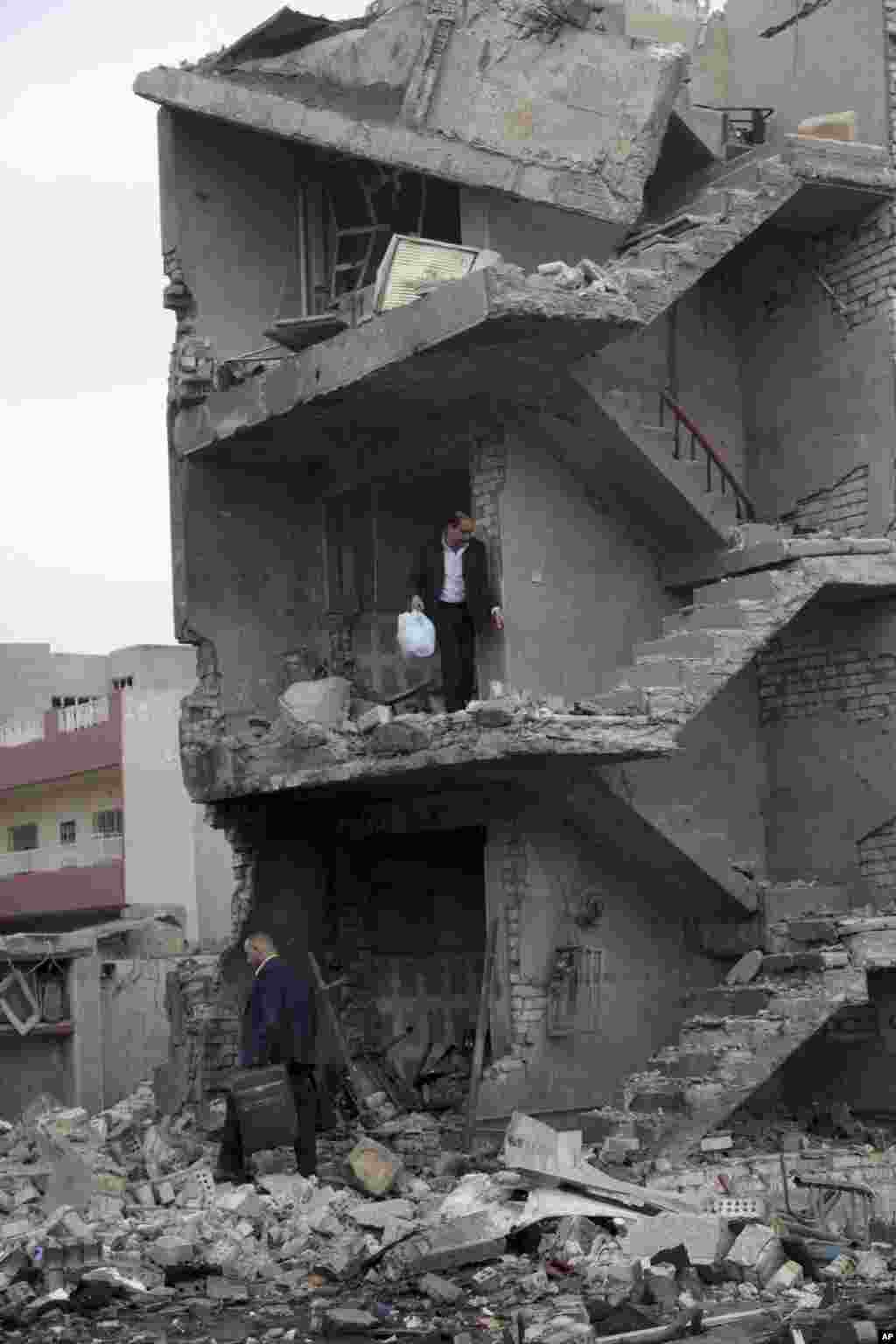 People collect their belongings from a heavily damaged building in the aftermath of a car bomb explosion in a commercial area of New Baghdad, Iraq. Gunmen stormed into a Baghdad mall on Monday after setting off a car bomb and launching a suicide attack at its entrance in the city&rsquo;s mainly Shiite east.