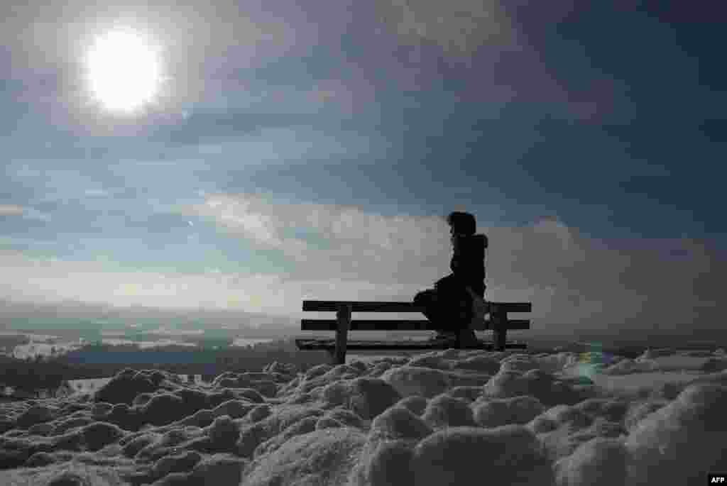 A young girl sits on a bench and enjoys the sunny winter weather with temperatures close to the freezing point in a snowy landscape near the small Bavarian village of Irschenberg, southern Germany.