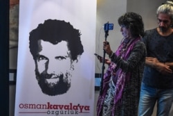 FILE - A journalist stands in front of a poster featuring jailed philanthropist Osman Kavala, during a press conference given by his lawyers, in Istanbul, Turkey, Oct. 31, 2018. Kavala was among those acquitted Tuesday.