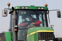 A French farmer, wearing a protective face mask, gives a driving lesson to a new young farm worker for his tractor in Anneux, France, March 27, 2020.