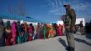 Voters line up to cast their votes as an Indian security officer stands guard outside a polling station during the last phase of the Jammu and Kashmir state assembly elections on the outskirts of Jammu, Dec. 20, 2014.