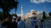 FILE - People use their mobile phone to take a selfie outside the Byzantine-era Hagia Sophia, one of Istanbul's main tourist attractions in the historic Sultanahmet district of Istanbul, Turkey, July 11, 2020.