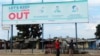 FILE - Two men stand underneath a giant poster showing advice on how to prevent the spread of the coronavirus, in Harare, Zimbabwe, April, 5, 2020. 