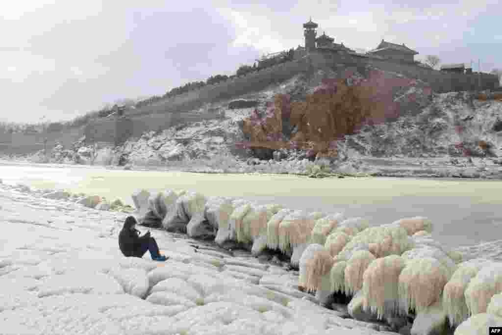 A person takes photos of ice on the rocks by the seaside in Penglai, in eastern China&#39;s Shandong province.