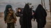 Veiled women, reportedly wives and members of the Islamic State, walk under the supervision of a female fighter from the Syrian Democratic Forces (SDF) at al-Hol camp in al-Hasakeh governorate in northeastern Syria, Feb. 17, 2019.