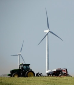 FILE - A farmer plants corn against a backdrop of wind turbines, June 8, 2019, in a field near Vesper, Kan.