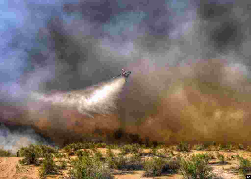 This photo provided by the San Bernardino County Fire Department shows a helicopter making a drop on a wildfire that started in western Arizona and jumped the Colorado River into California, near Needles, California, April 6, 2016.