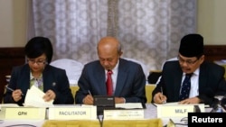 Government of the Philippines (GPH) chief negotiator Miriam Coronel Ferer (L) and Moro Islamic Liberation Front (MILF) chief negotiator Mohagher Iqbal (R) sign the peace agreement between both parties with AB Ghafar Tengku Mohamed as a witness from Malays