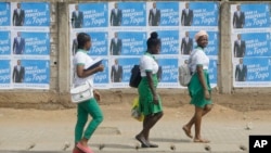 FILE - Schoolgirls walk past election posters of Togo's incumbent President Faure Gnassingbe, presidential candidate of Union for the Republic, on the street in Lome, Togo, Feb. 21, 2020.